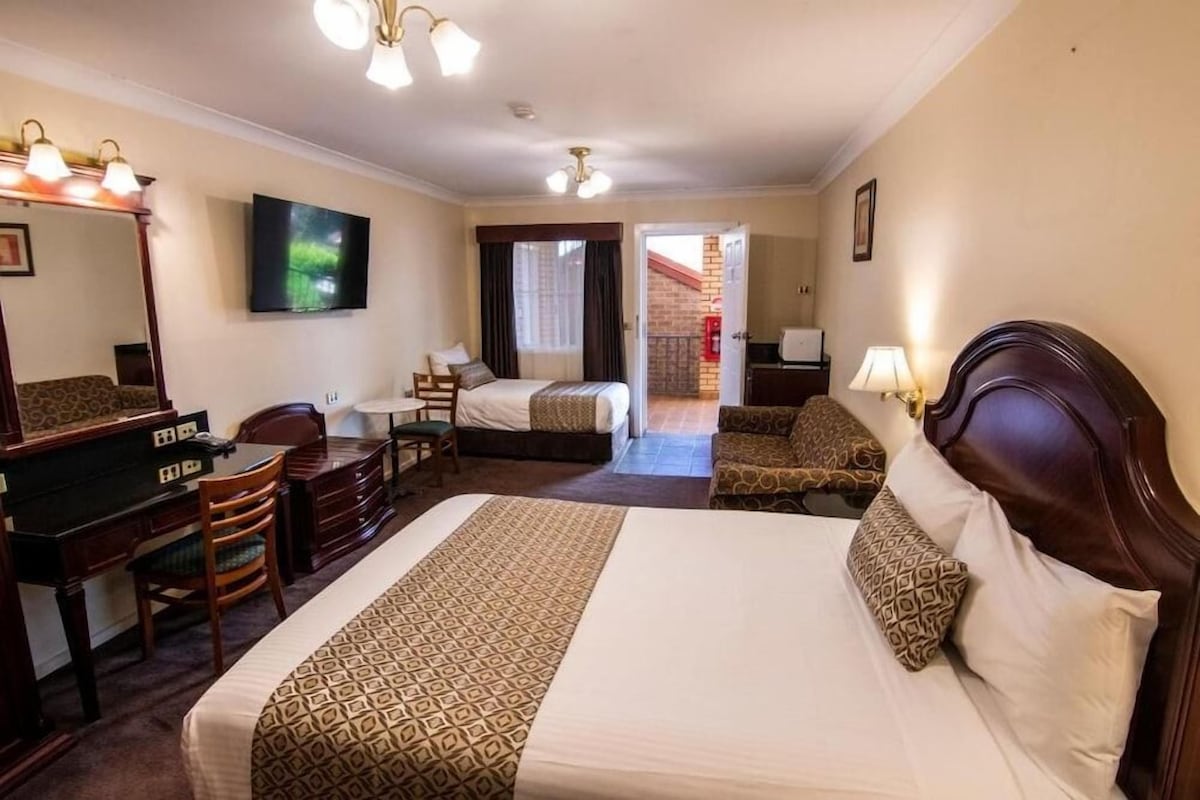 A hotel room with a large bed, a desk, a chair, a TV, and a door leading to another room.