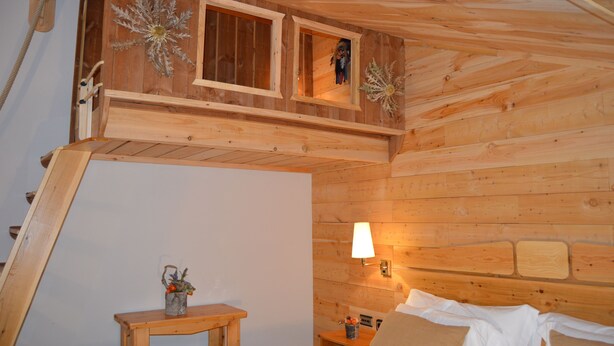 A wooden cabin interior with a bed, a small table with a plant, and a window with a view. - Hotel Coma Bella (Sant Julia de Loria)