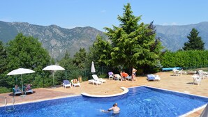 A swimming pool with lounge chairs and umbrellas, surrounded by trees and mountains in the background. - Hotel Coma Bella (Sant Julia de Loria)