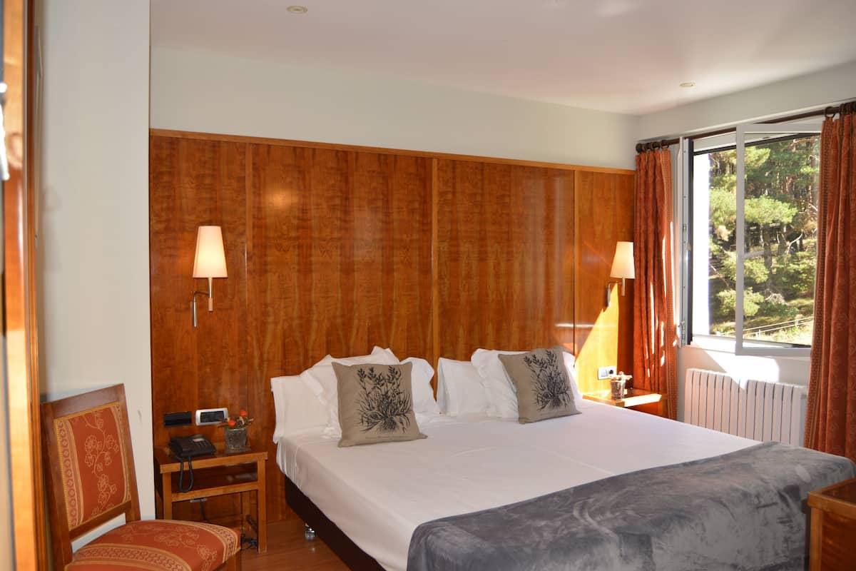 A hotel room with a large bed, wooden headboard, two bedside lamps, a nightstand with a telephone, and a window with curtains.