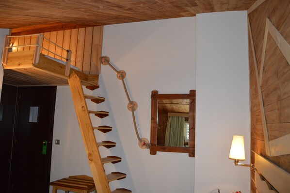 A wooden staircase with a handrail leading to a lofted area, a mirror on the wall, and a lamp on the floor. - Hotel Coma Bella (Sant Julia de Loria)