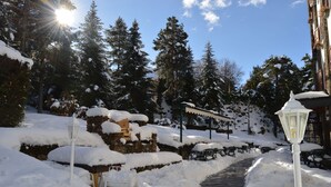 A snow-covered pathway leading to a building with a stone wall and a wooden bench. - Hotel Coma Bella (Sant Julia de Loria)