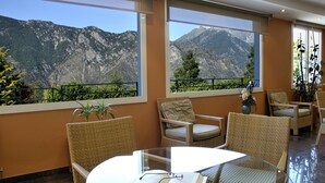 A room with a glass table, wicker chairs, and a view of mountains through large windows. - Hotel Coma Bella (Sant Julia de Loria)