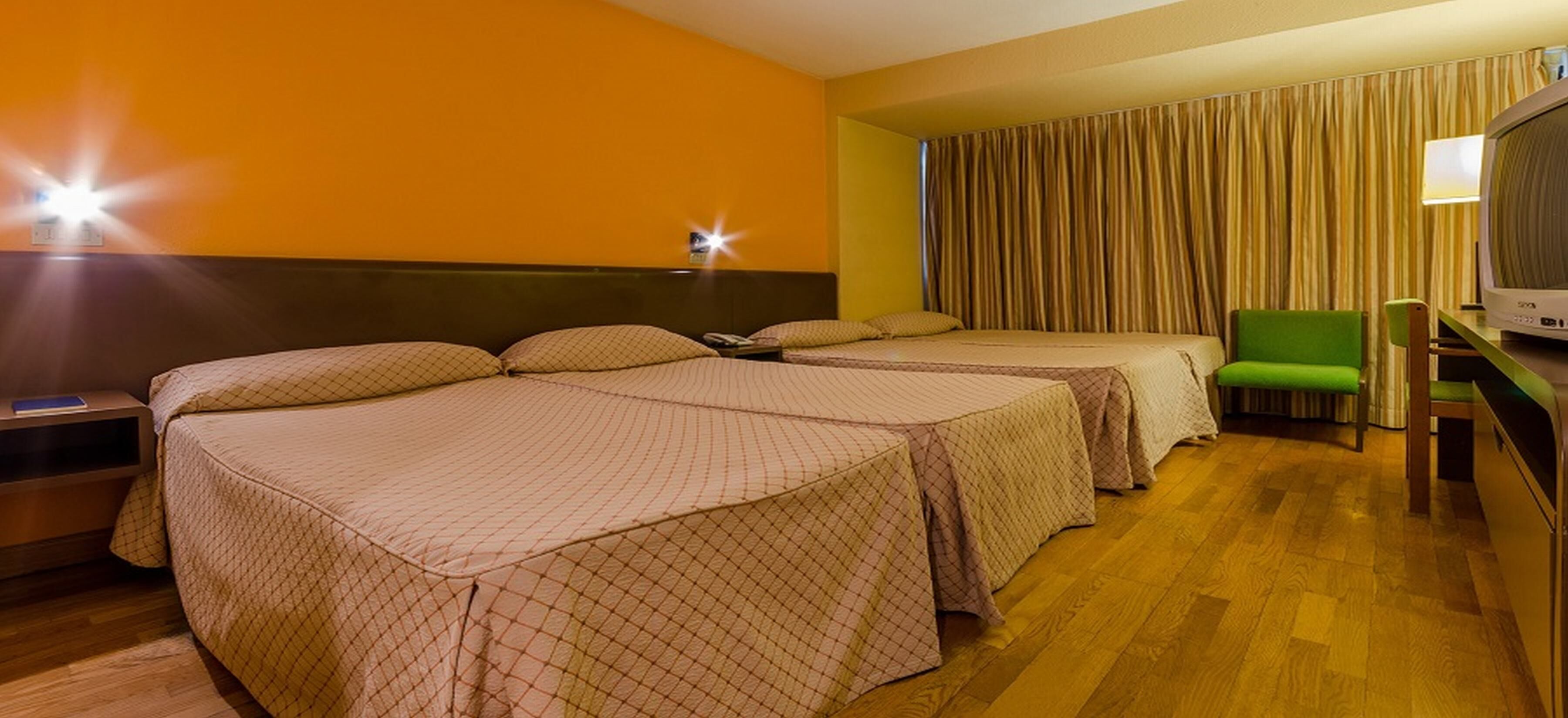 Une chambre d’hôtel avec deux lits, une télévision, un fauteuil vert et un rideau.