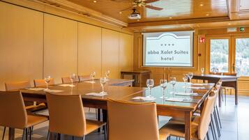 A conference room with a large table and chairs, a ceiling fan, and a projection screen displaying the hotel name.