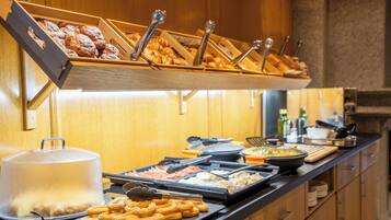 Een buffet met diverse gerechten, waaronder gebak en een afgedekte schaal, in een kamer met houten lambrisering.