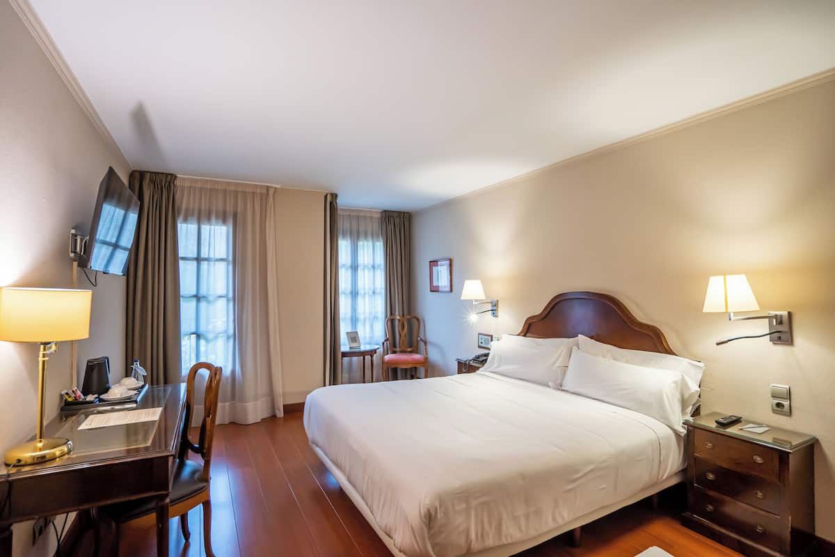 A hotel room with a bed, desk, chair, TV, and bedside lamps.