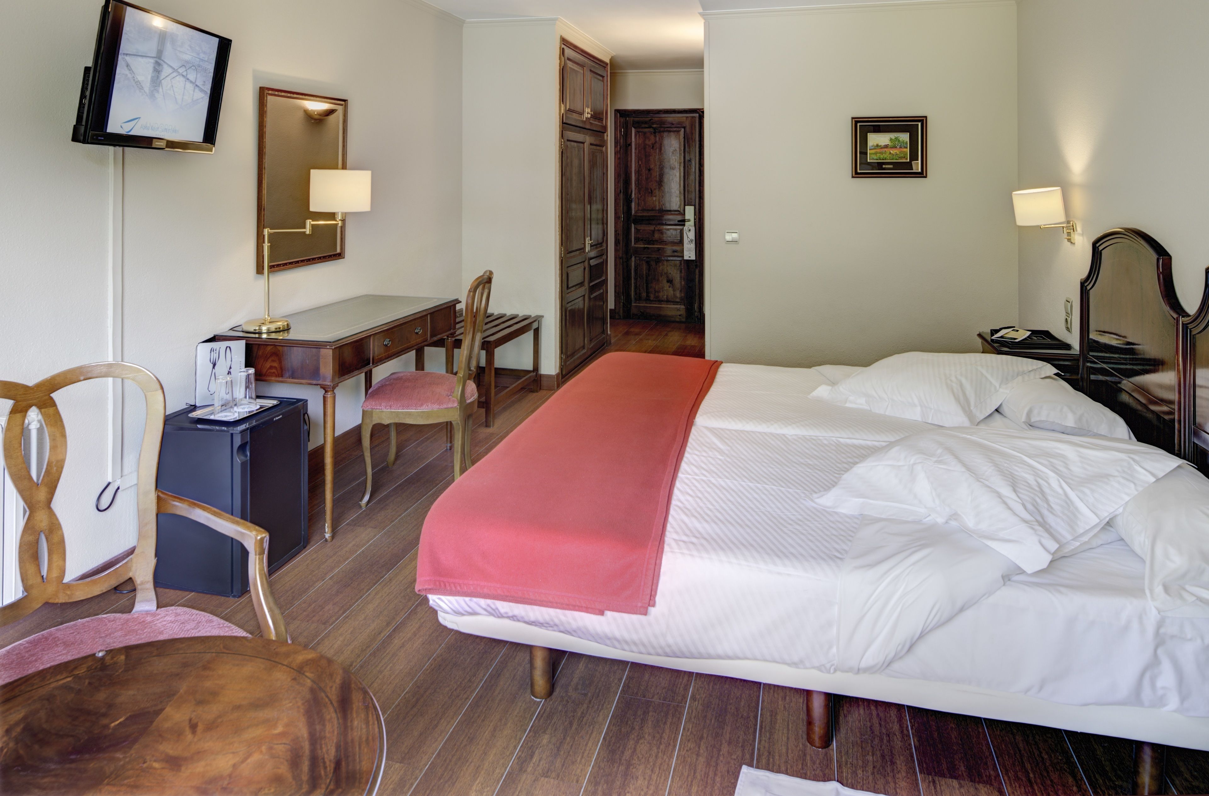 A hotel room with a bed, desk, chair, and a television.