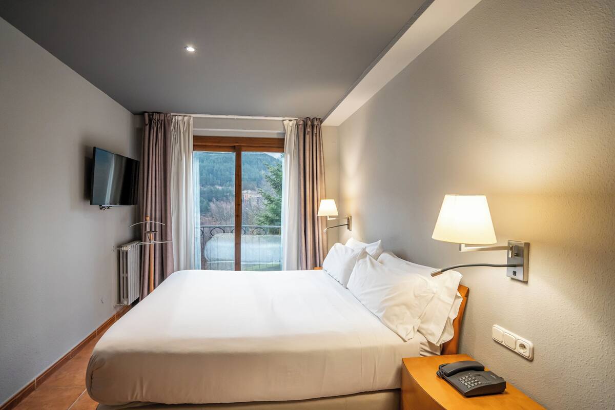 A hotel room with a large bed, a television mounted on the wall, a bedside lamp, and a telephone on the nightstand.