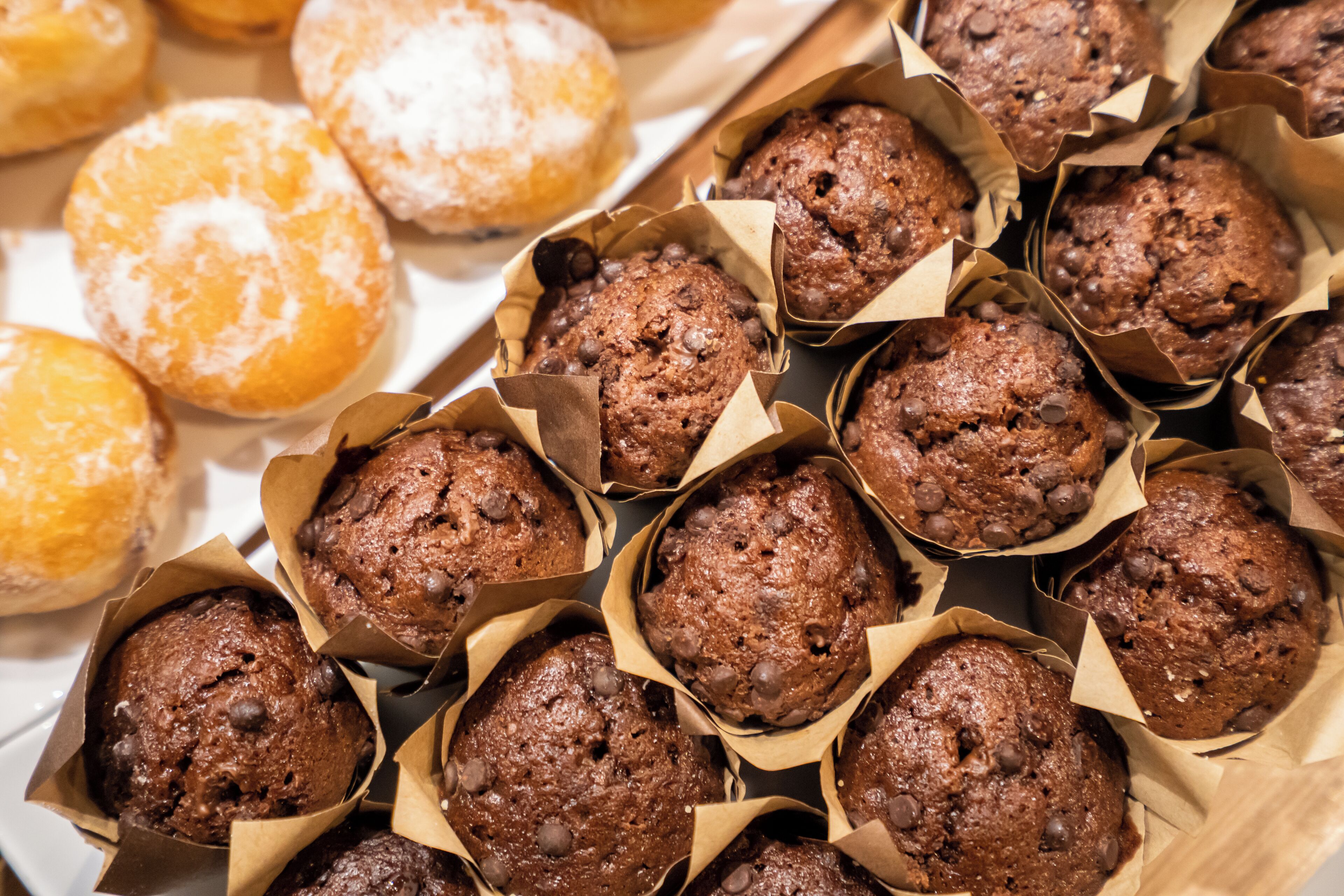 Una bandeja con varios productos horneados, como muffins de chips de chocolate y donas con azúcar glas.