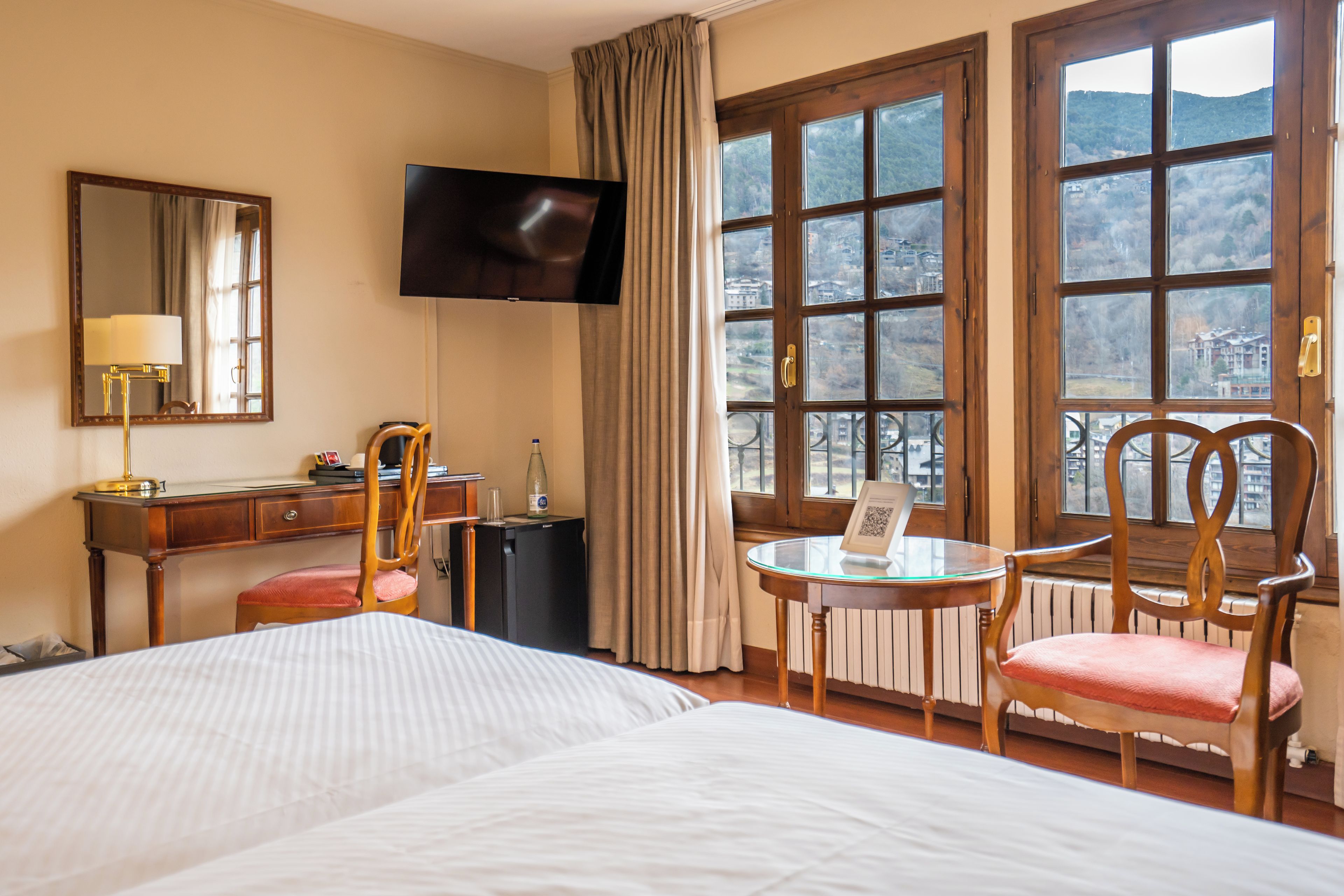 Une chambre d’hôtel comprenant un lit, un bureau, une chaise, un téléviseur, une fenêtre avec vue et une table avec un plateau en verre.