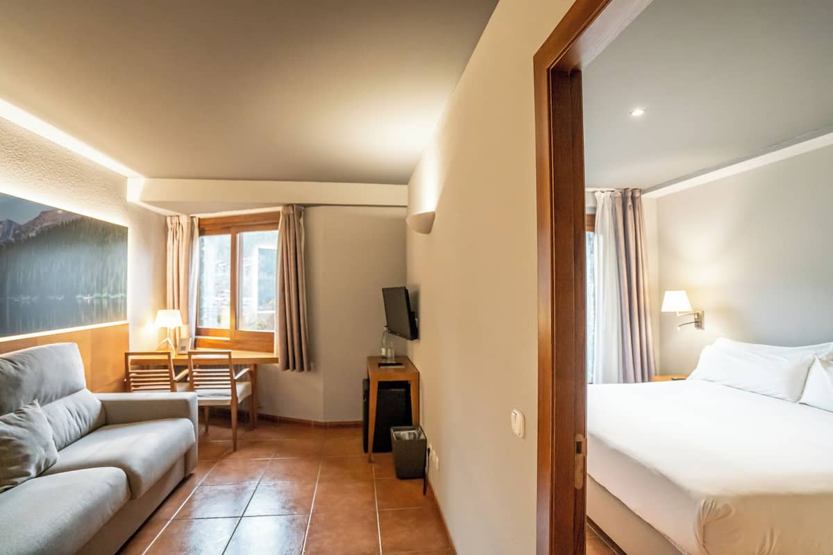 A hotel room with a bed, a sofa, a desk, a TV, and a window with curtains.