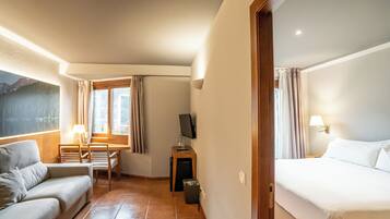 A hotel room with a bed, a sofa, a desk, a TV, and a window with curtains.