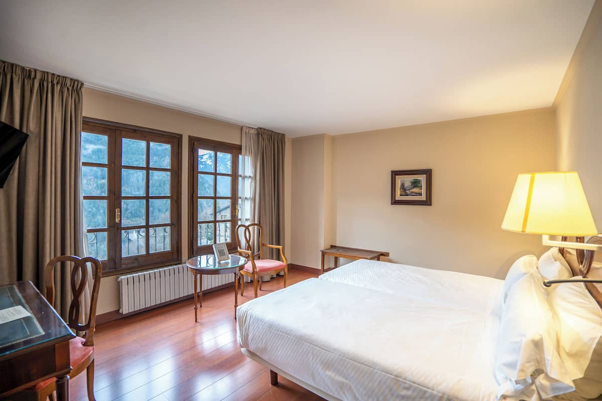 A hotel room with a bed, a desk, a chair, a table, and a lamp.