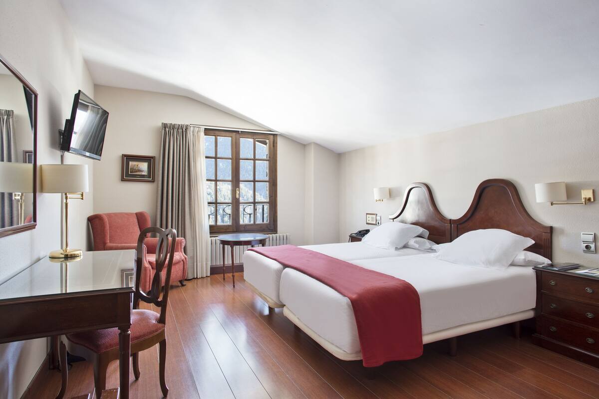 A hotel room with a large bed, a desk with a chair, a television, and a window with curtains.