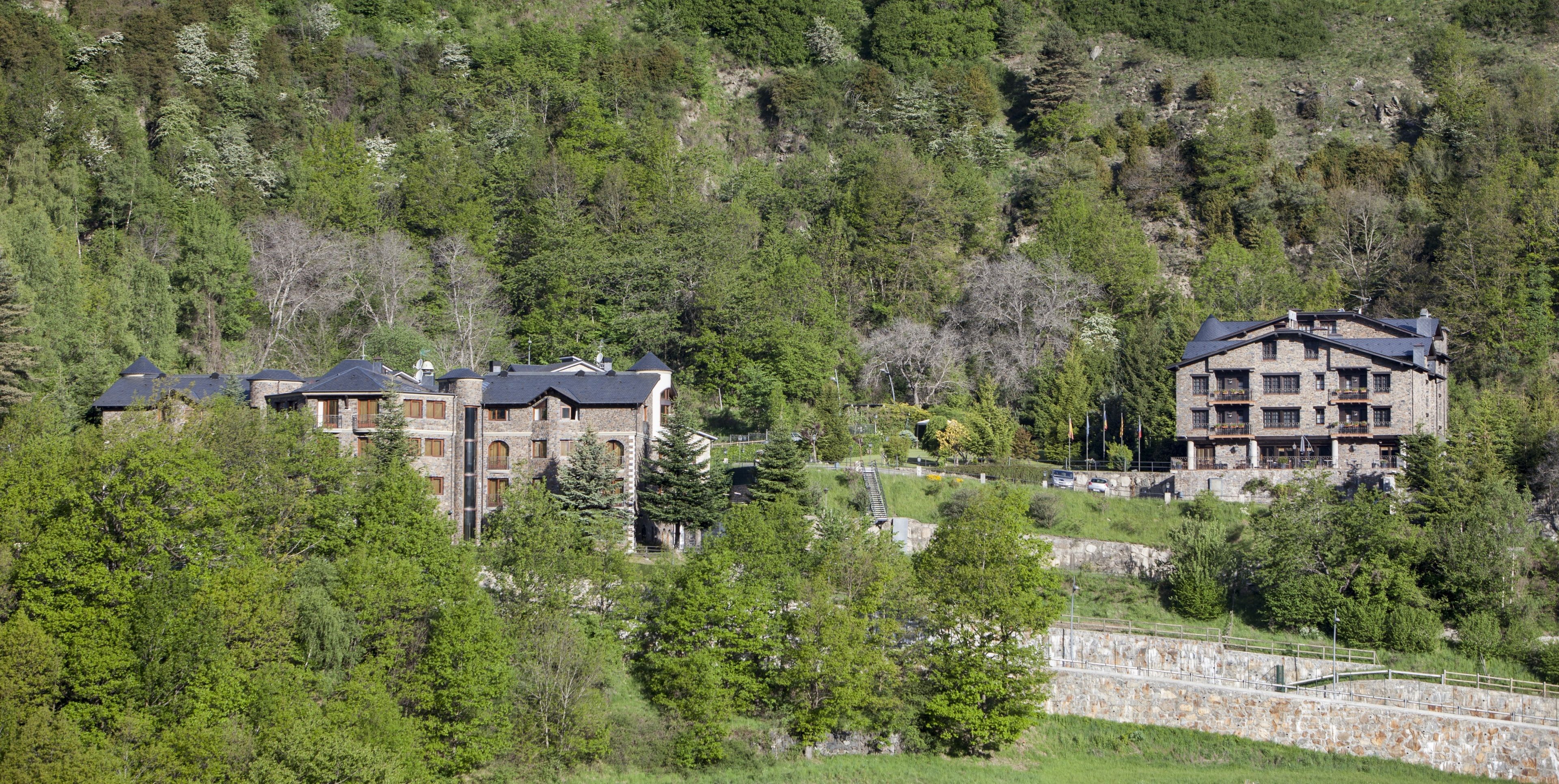 A multi-story building with a stone facade and multiple balconies, surrounded by dense forest.