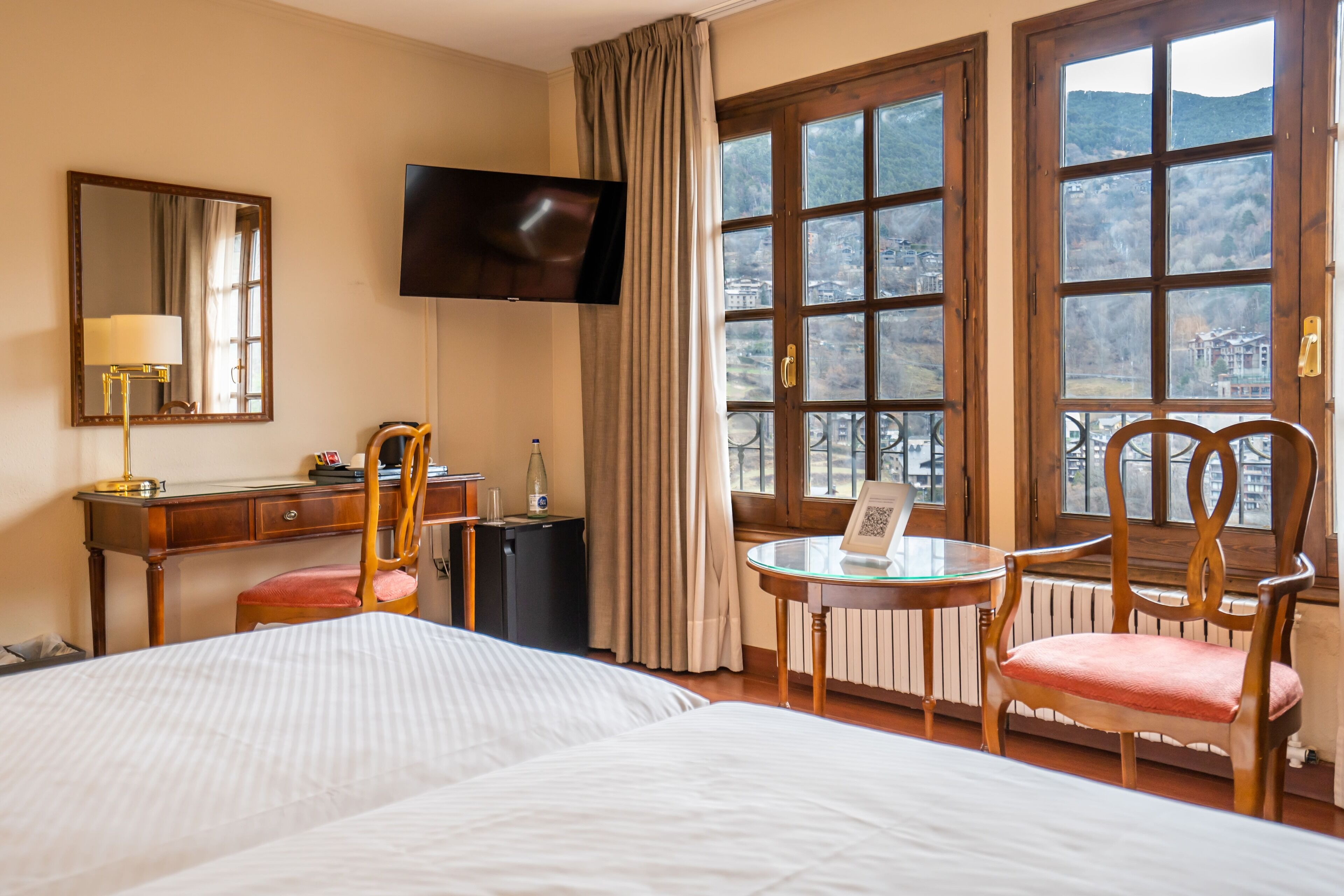 Habitación de hotel con cama, escritorio, silla, televisor, ventana con vistas y una mesa con una silla.