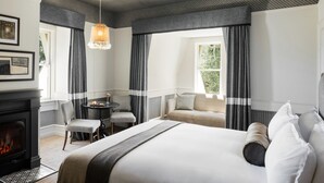 Habitación de hotel con una cama grande, chimenea, sofá, mesa de comedor y vistas al exterior.