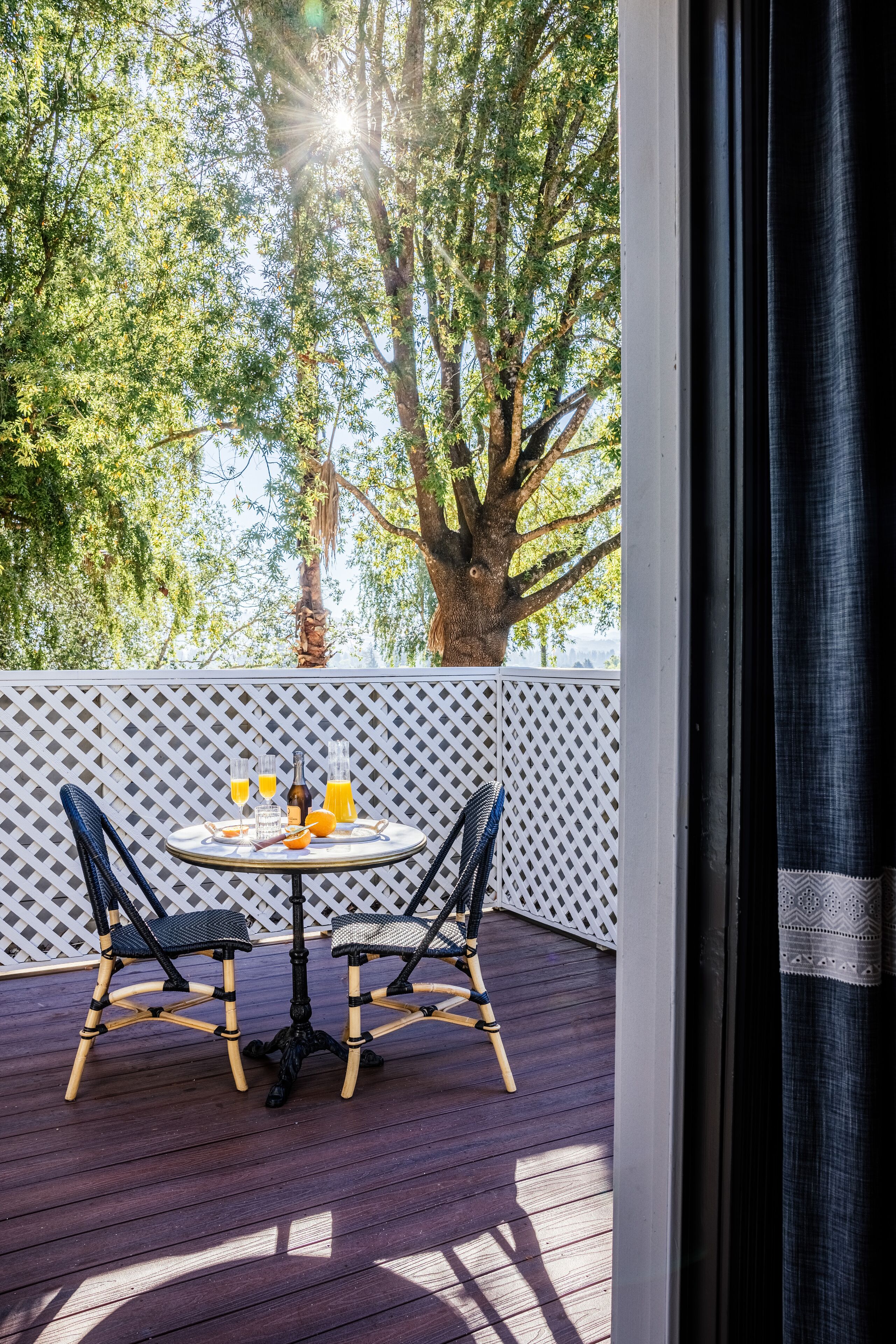 A wooden deck with a table and chairs, a bottle, and glasses of orange juice.