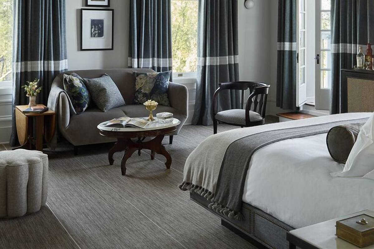A bedroom with a large bed, a sofa, a chair, and a small table. There are curtains on the windows, and a chandelier hangs from the ceiling.