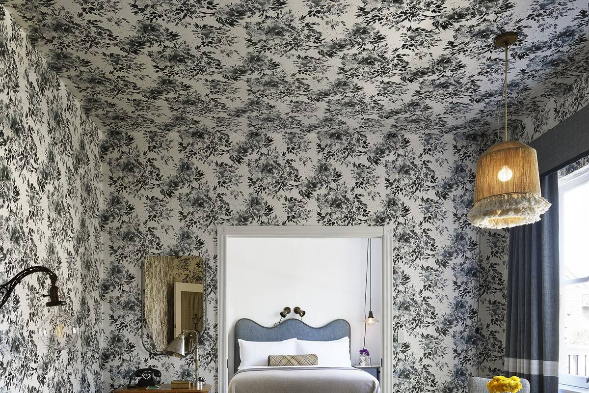 A room with floral wallpaper, a bed with a headboard, a sofa, a coffee table, and a dining table with chairs.