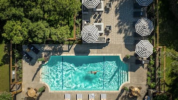 An aerial view of a swimming pool area with multiple lounge chairs and umbrellas, surrounded by lush greenery.