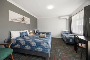 Ett hotellrum med två sängar, ett skrivbord, en stol och ett stort fönster med gardiner.