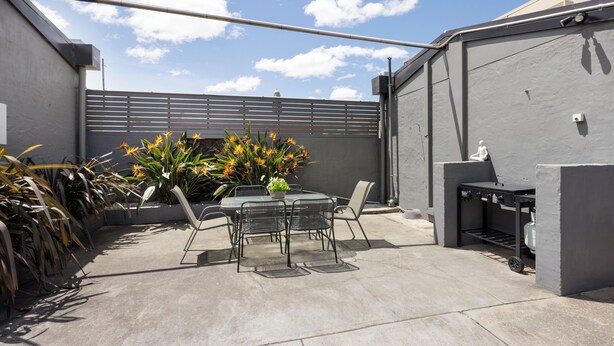 An outdoor patio with a table and chairs, a grill, and potted plants. - Castle Motel Bairnsdale (Bairnsdale)
