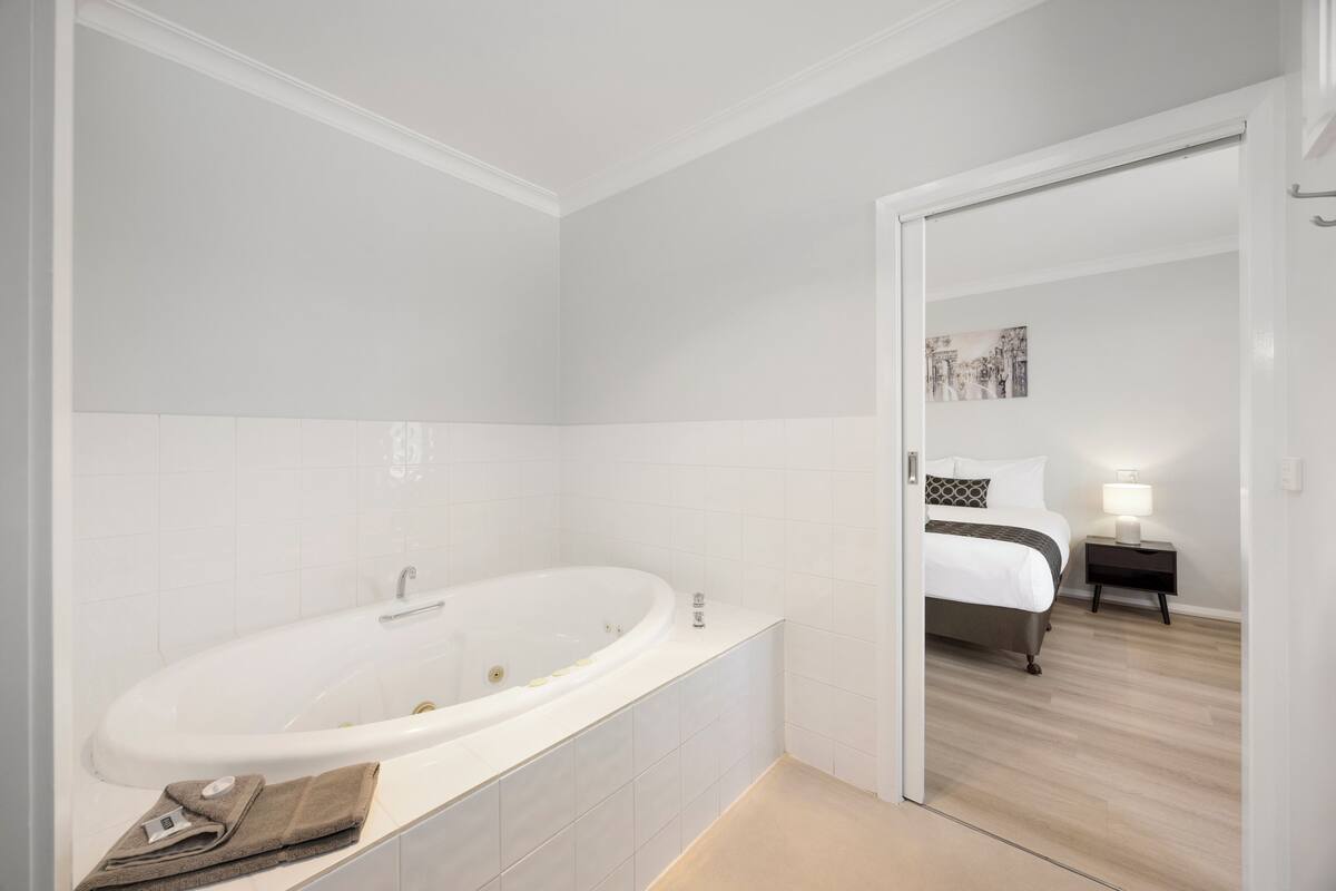 A modern bathroom with a large bathtub, a mirror, and a towel rack.