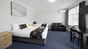 A hotel room with two beds, a desk, a chair, a sofa, and a painting on the wall. - Castle Motel Bairnsdale (Bairnsdale)