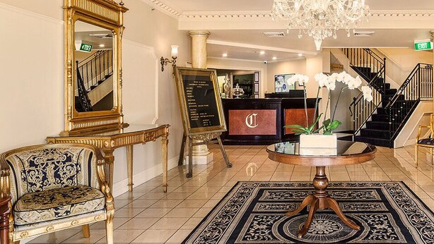 A grand lobby with a chandelier, a reception desk, a staircase, and classic furniture. - Canterbury International Hotel (Forest Hill)