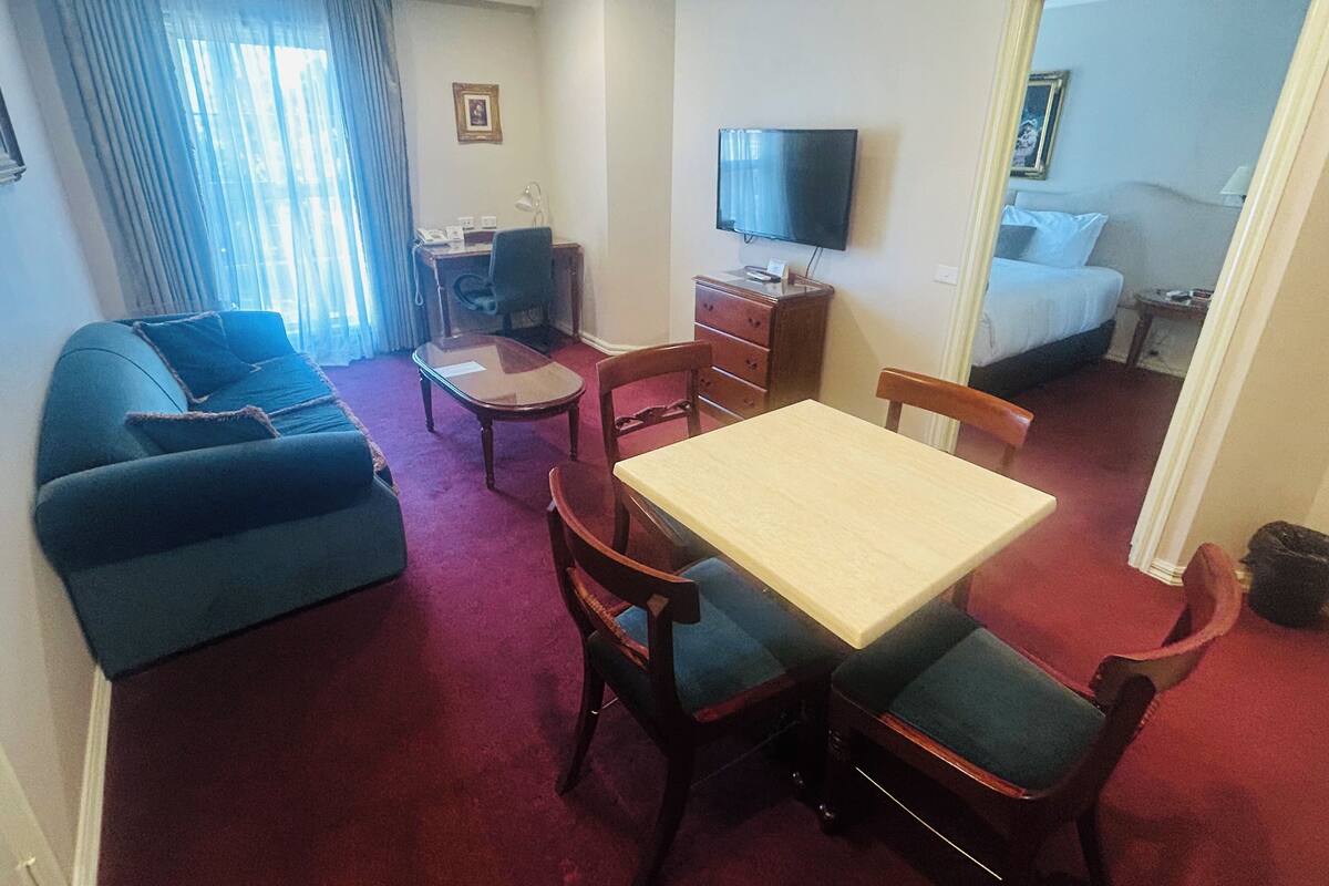 Habitación de hotel con sofá, mesa de comedor con sillas, televisor, escritorio y cama.