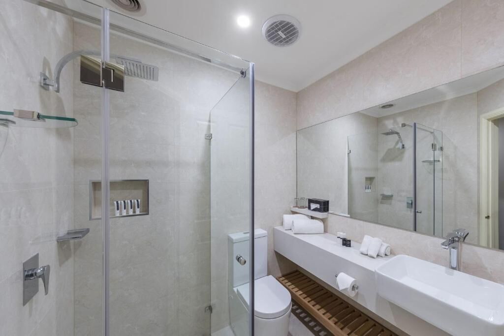 A modern bathroom with a glass-enclosed shower, a toilet, a sink, and a mirror.