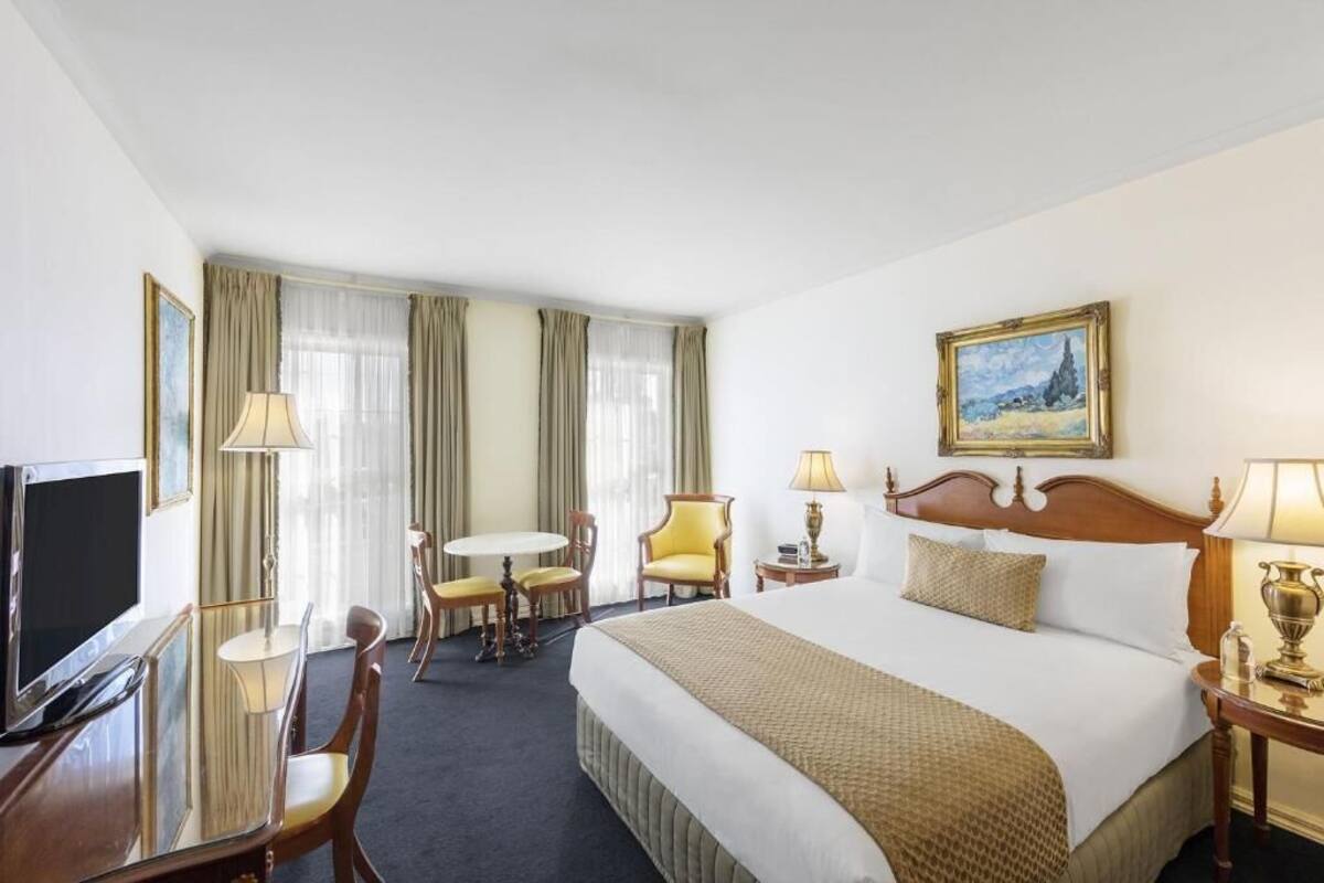 Una habitación de hotel con cama, escritorio, silla, televisor y un cuadro en la pared.