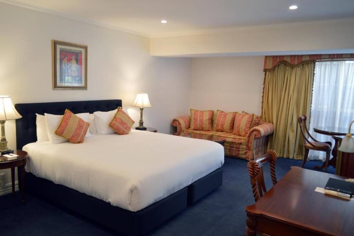 Una habitación de hotel con una cama grande, un sofá, una mesa de comedor y una lámpara.