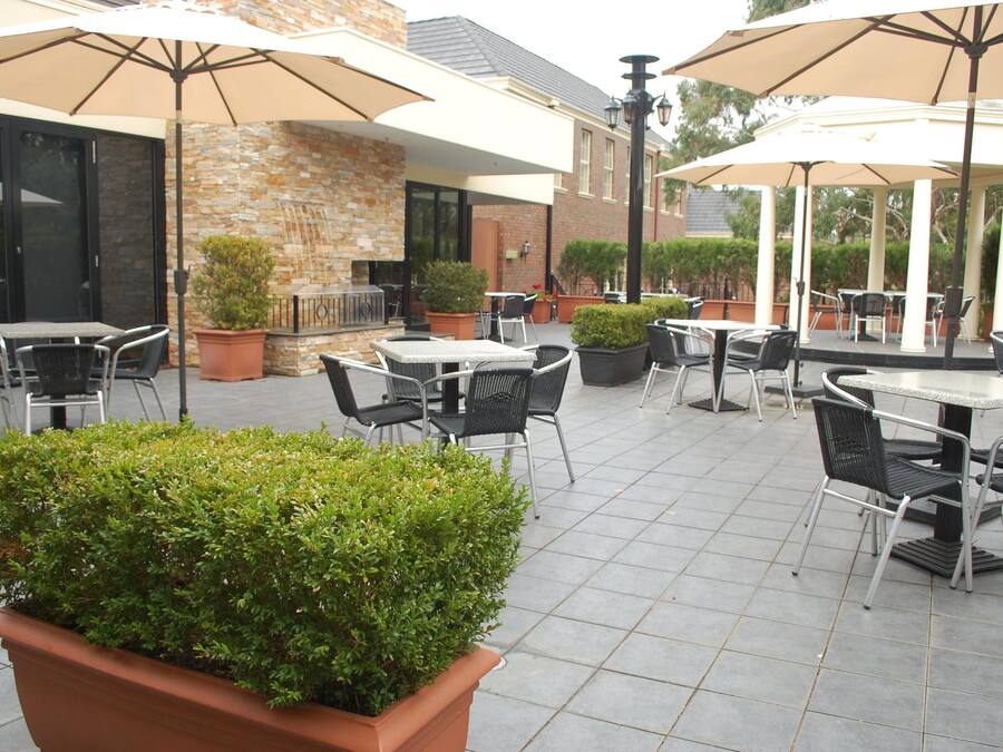 An outdoor patio area with multiple tables and chairs, surrounded by potted plants and umbrellas.
