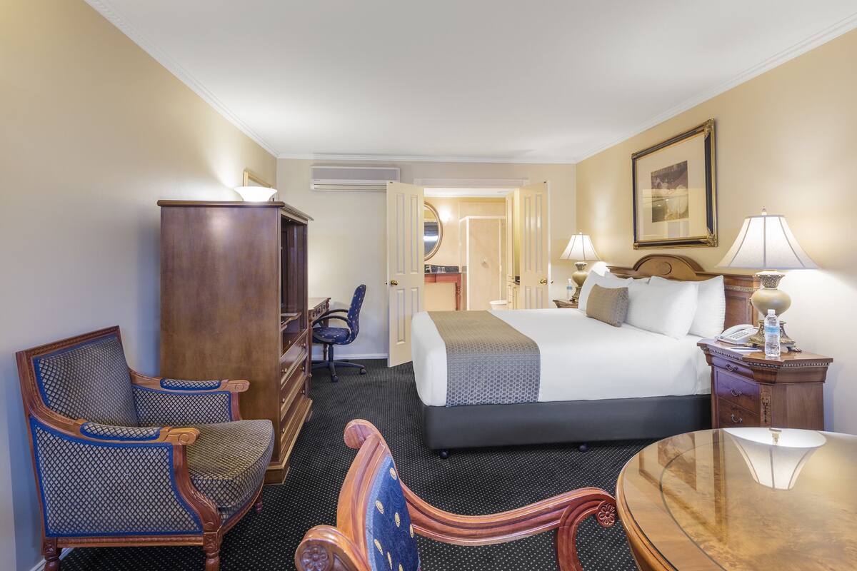 Una habitación de hotel con una cama, dos sillas, un escritorio, una lámpara y una mesita de noche.