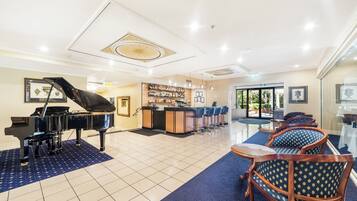 A hotel lobby with a grand piano, a bar area, and seating with a blue patterned rug.
