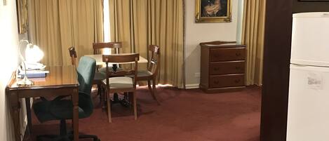 Habitación de hotel con zona de comedor, escritorio con lámpara, una silla, un armario pequeño y microondas.