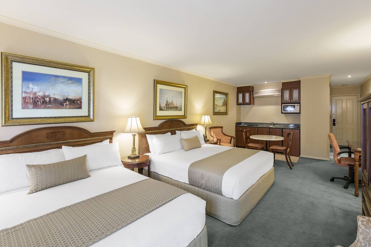 Habitación de hotel con dos camas, un escritorio, una silla, una mesita y un televisor.