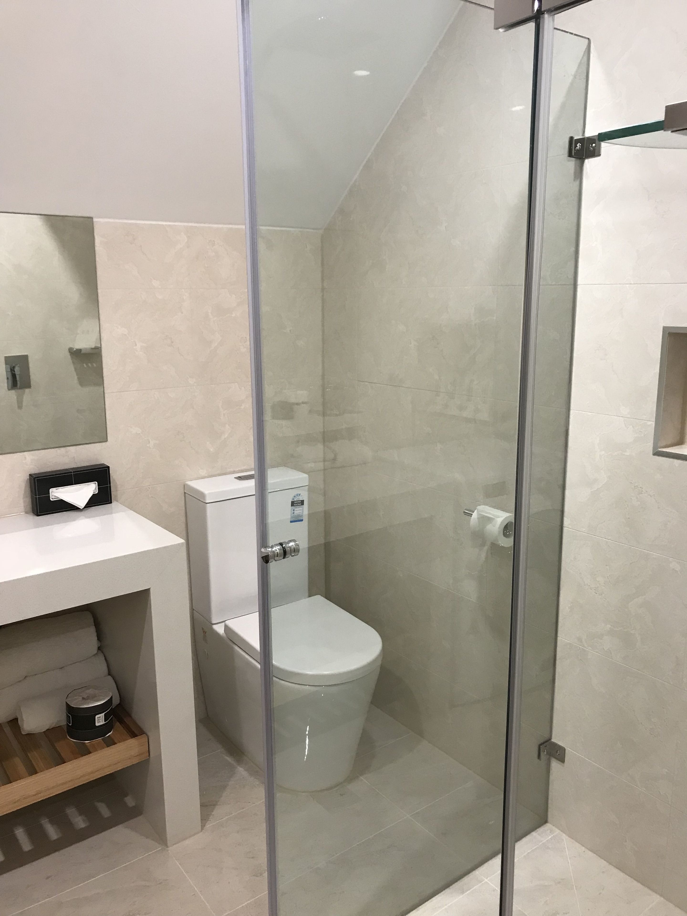 Een moderne badkamer met een douchecabine van glas, een wit toilet en een wastafel met een tissuedoos.