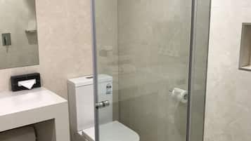 Een moderne badkamer met een douchecabine van glas, een wit toilet en een wastafel met een tissuedoos.