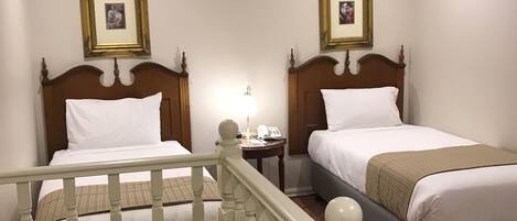 Habitación de hotel con dos camas individuales, una mesita de noche pequeña con lámpara y un cuadro en la pared.