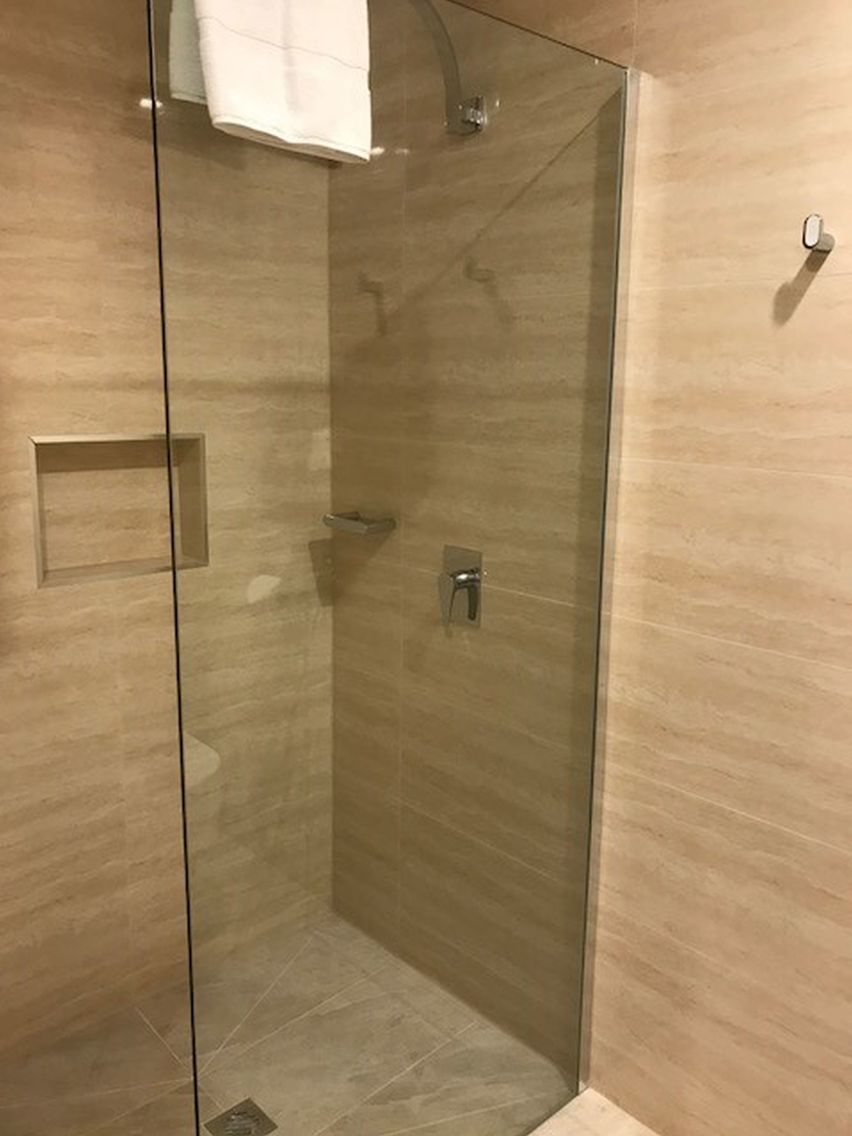 En duschkabin med glasväggar, där en handduk hänger på väggen, samt en kontrollpanel och en liten hylla.