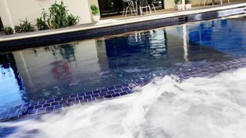 An indoor swimming pool with a tiled edge, a lifebuoy on the wall, and a seating area with chairs and tables.