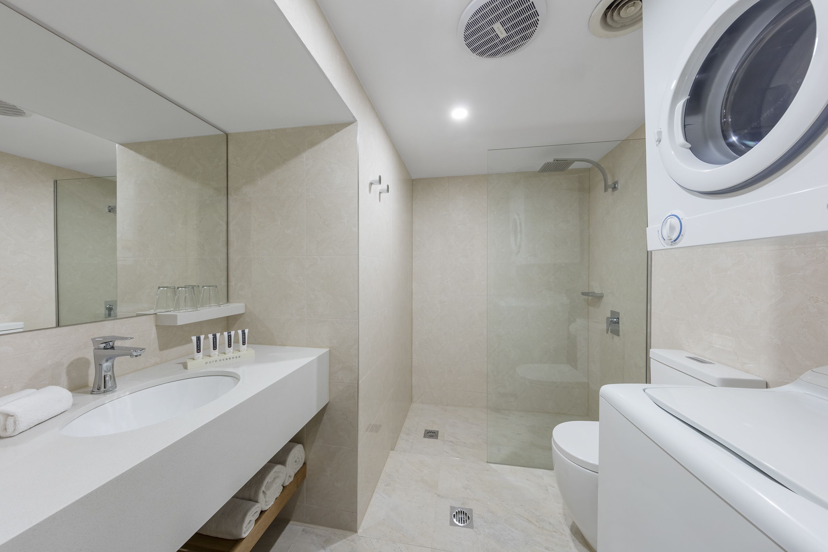 Un baño moderno con un espejo grande, dos lavamanos, un inodoro y una lavadora integrada.
