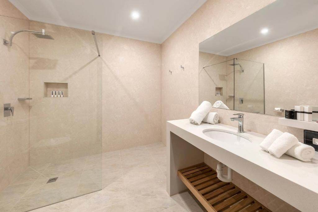 Un baño moderno con ducha envuelta en vidrio, un espejo grande y un mueble de tocador de madera.