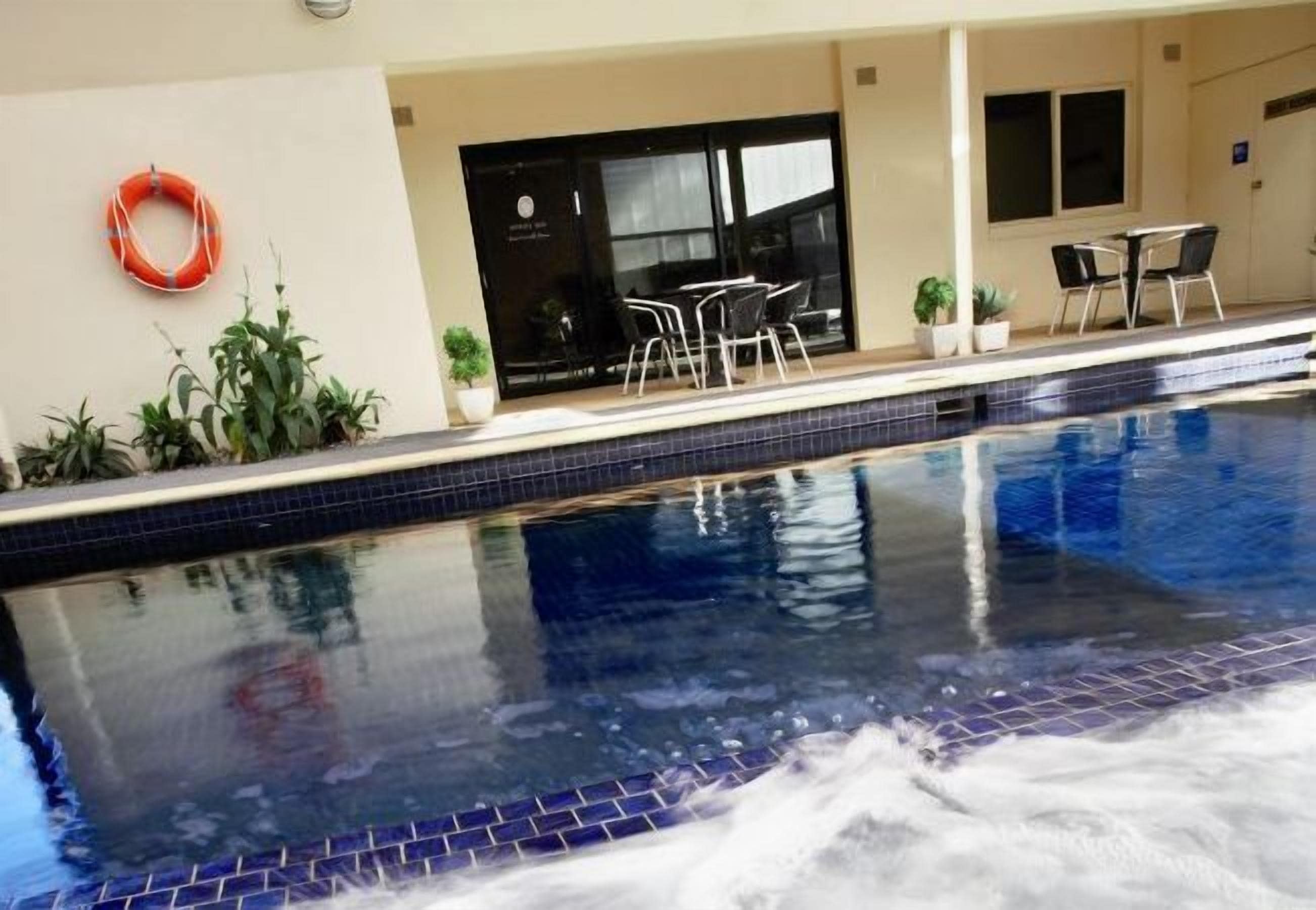 Une piscine dont le bord est revêtu de carreaux, entourée de plantes en pot et agrémentée de mobilier d’extérieur.