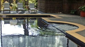 A swimming pool with a tiled edge, surrounded by chairs and a thatched wall. - Canterbury International Hotel (Forest Hill)