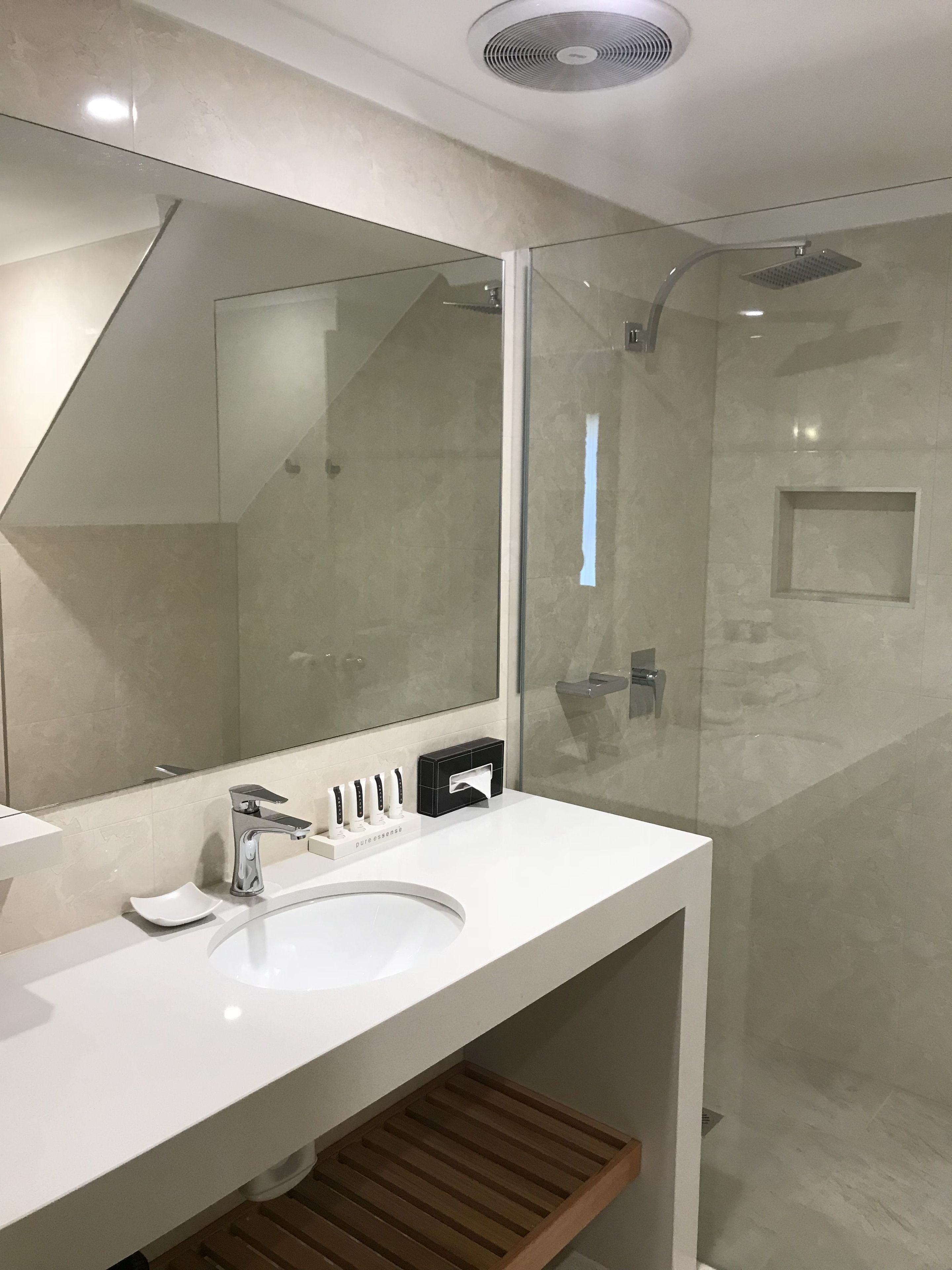 Un baño moderno con un lavamanos blanco, un espejo grande y una ducha con cerramiento de vidrio.